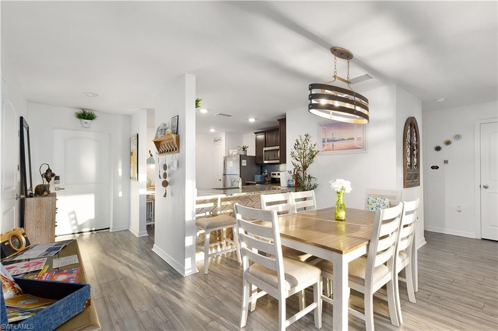 Wood-finish flooring throughout, a dining area with a contemporary chandelier, a breakfast bar, and a kitchen featuring dark wood cabinetry and stainless steel appliances