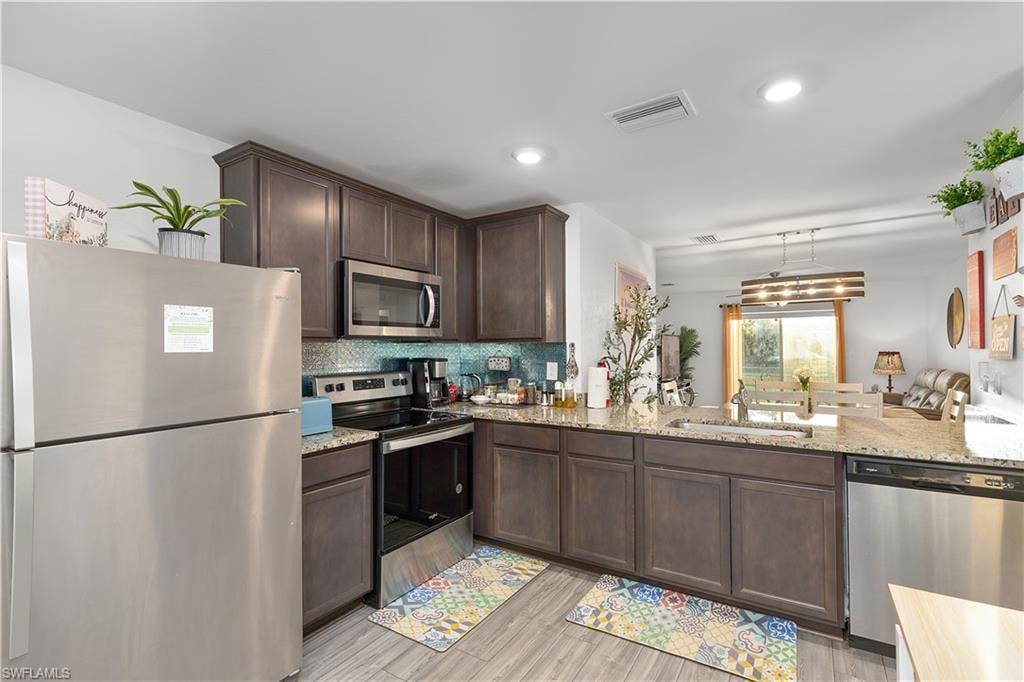 Kitchen with wood-finish flooring, dark wood cabinetry, stainless steel appliances, and light-colored countertops