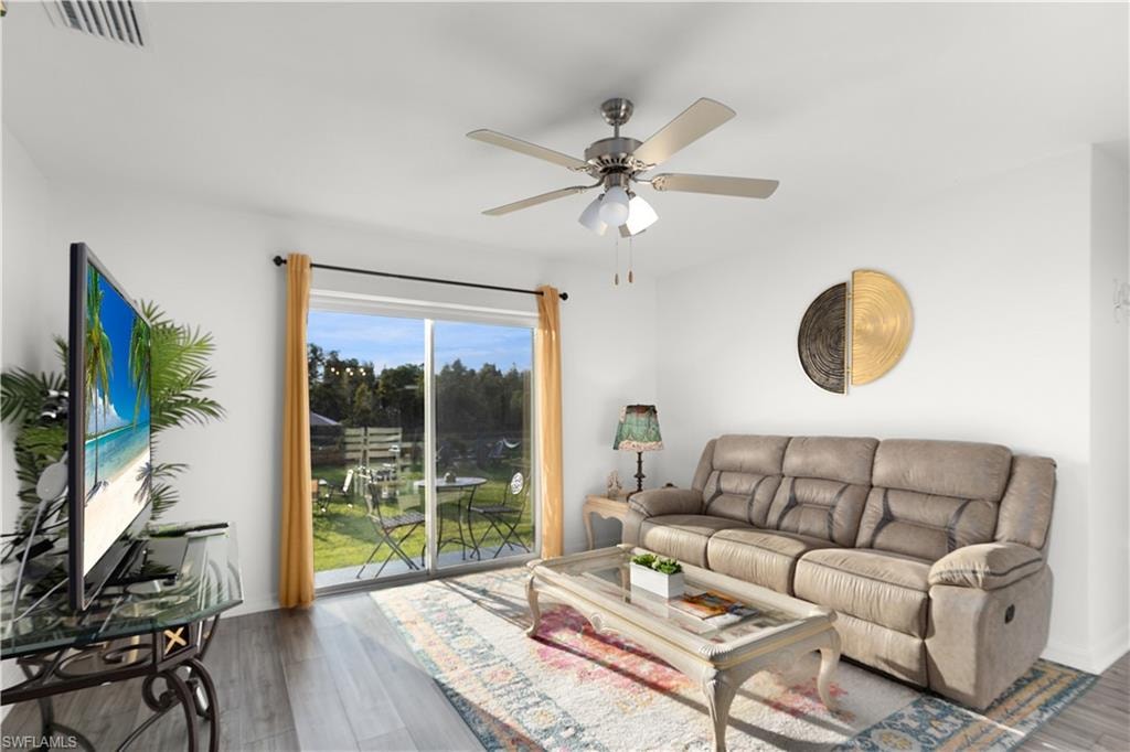 Sliding glass doors leading to an outdoor patio with a manicured lawn, wood-finish flooring, and a ceiling fan with integrated lighting