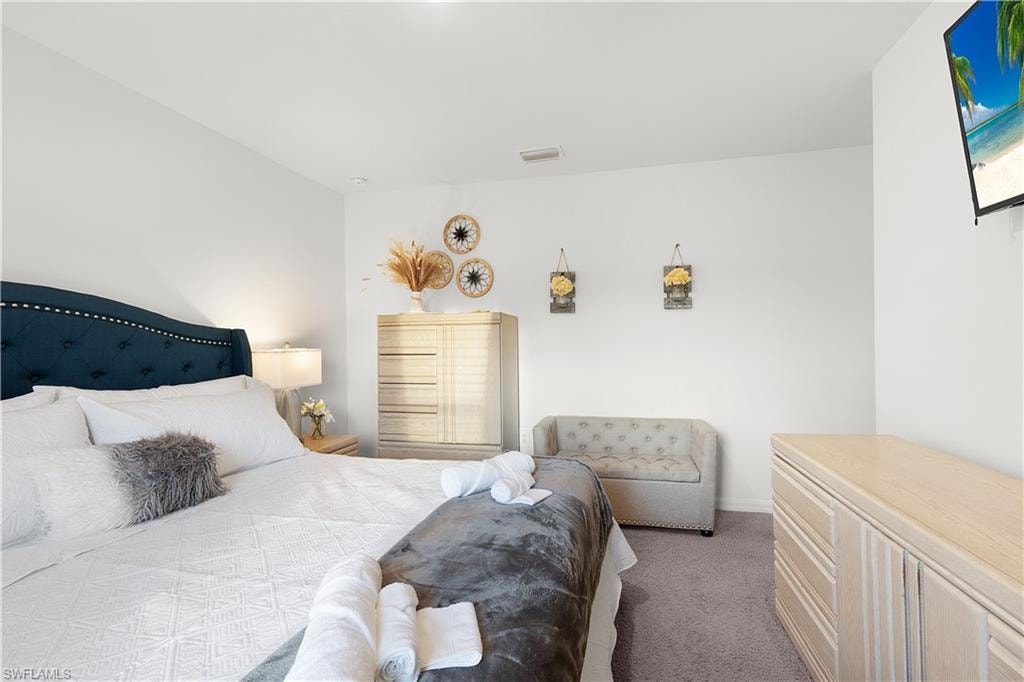 Tufted upholstered headboard, recessed lighting, wall-mounted television, light-toned wood-finish dresser, and light gray carpet