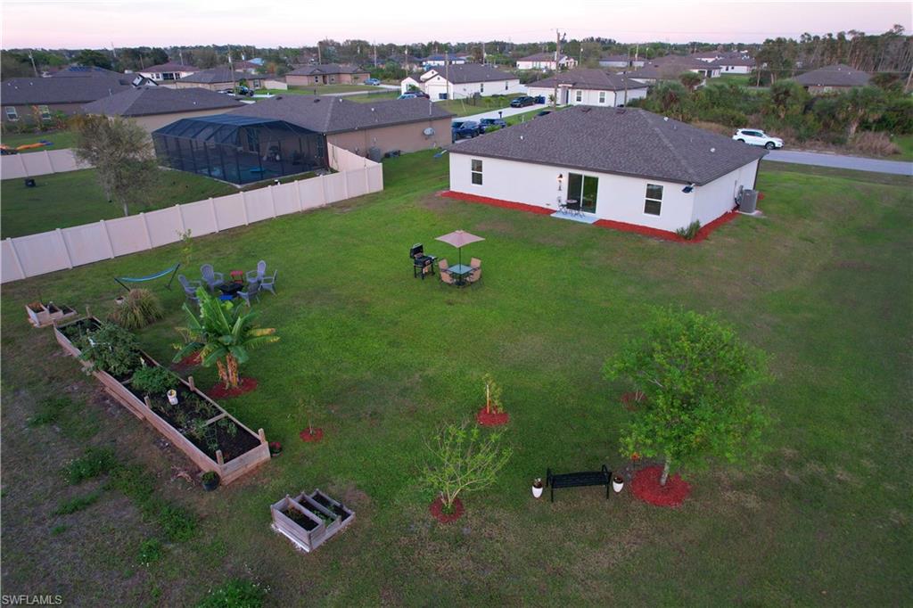 Expansive green lawn with a screened pool enclosure, privacy fence, and raised garden beds