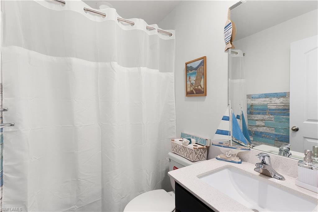 Bathroom with a vanity featuring a single basin sink, a wall-mounted mirror, and a shower curtain