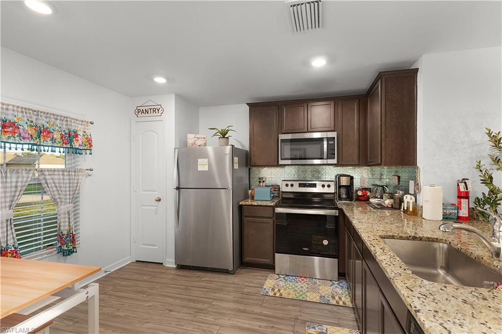 Kitchen featuring wood-finish flooring, stainless steel appliances, dark wood cabinetry, granite countertops, and a tiled backsplash
