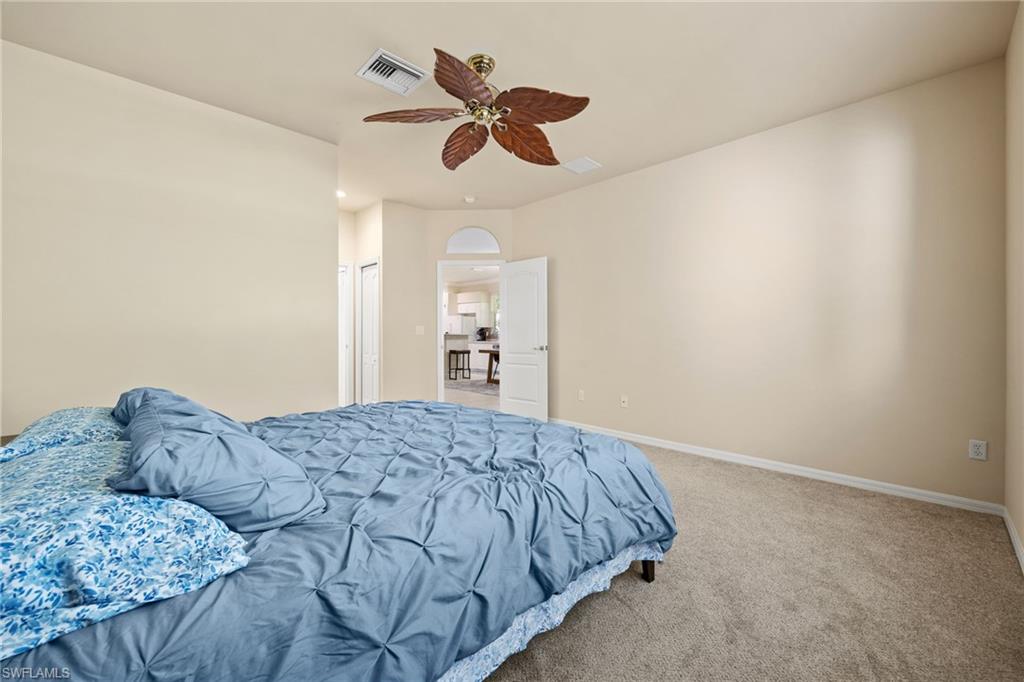 Spacious primary bedroom featuring neutral wall finishes, plush carpeting, and a ceiling fan with wood-finish blades