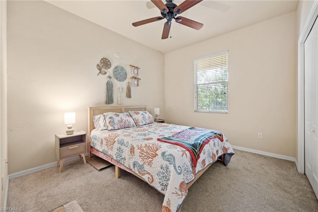 Bright secondary bedroom featuring neutral carpeting, a ceiling fan with wood-finish blades, and a large window with plantation shutters providing natural light