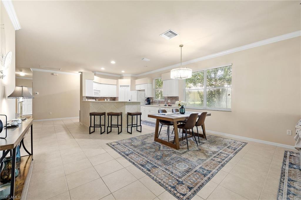 Open-concept living area featuring tile flooring throughout, a kitchen with white cabinetry and stainless steel appliances, a dining table with seating for multiple guests, and abundant natural light from multiple windows