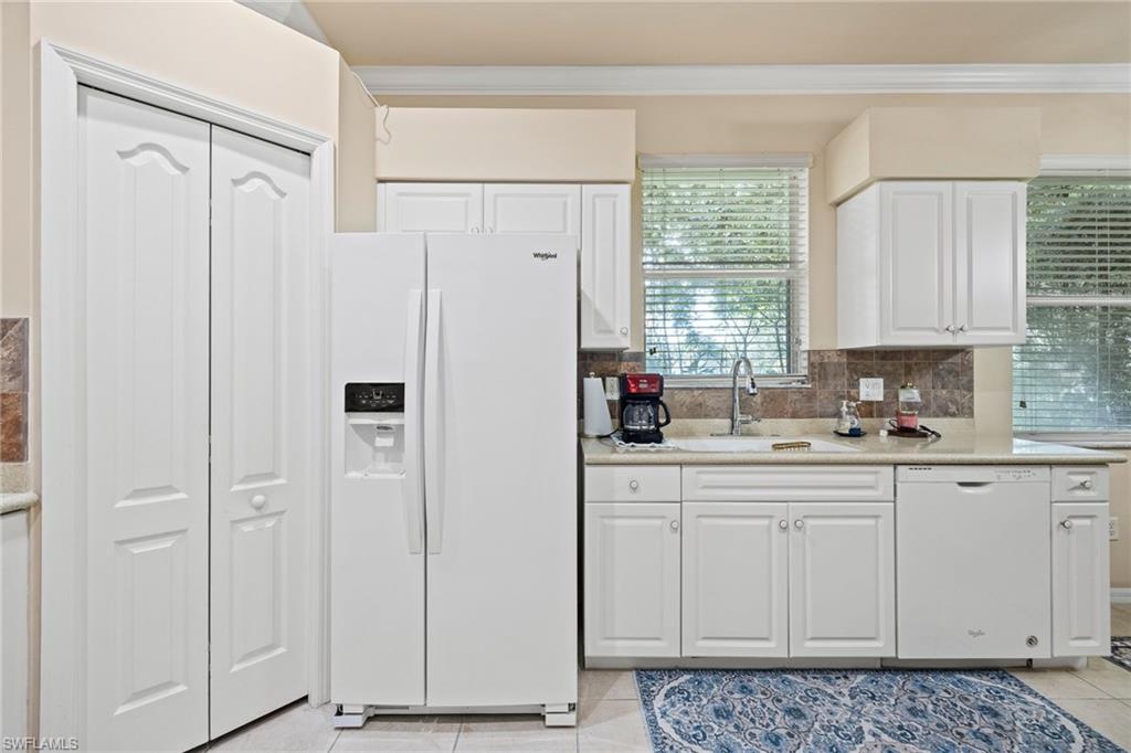 Bright, well-appointed kitchen featuring white cabinetry, stainless steel side-by-side refrigerator with ice and water dispensers, tile backsplash, and ample counter and storage space