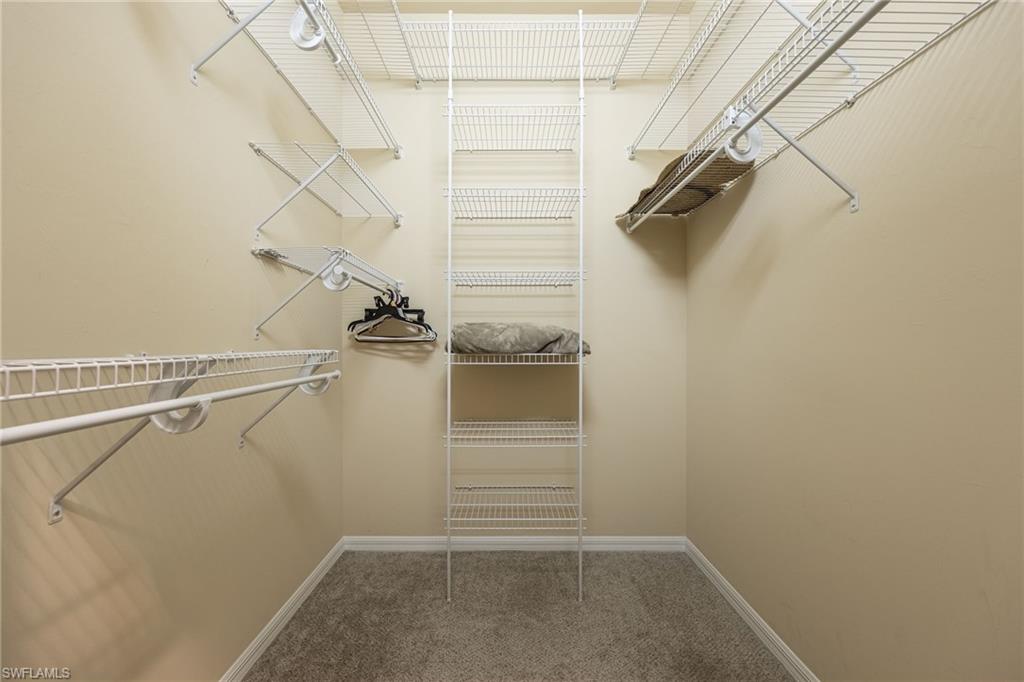 Spacious walk-in closet featuring multiple wire shelving units with adjustable brackets, dual clothing rods at varying heights, and carpeted flooring for comfortable organization and storage