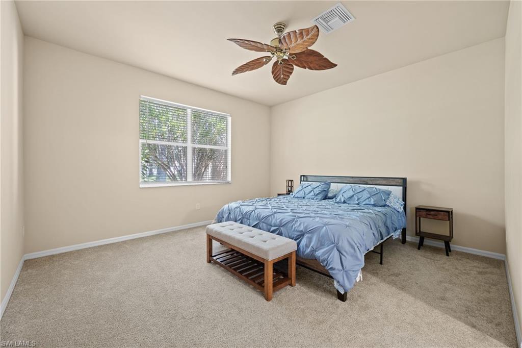 Spacious bedroom with neutral carpeting, large windows providing natural light, ceiling fan with integrated lighting, and wood-frame bed with blue bedding