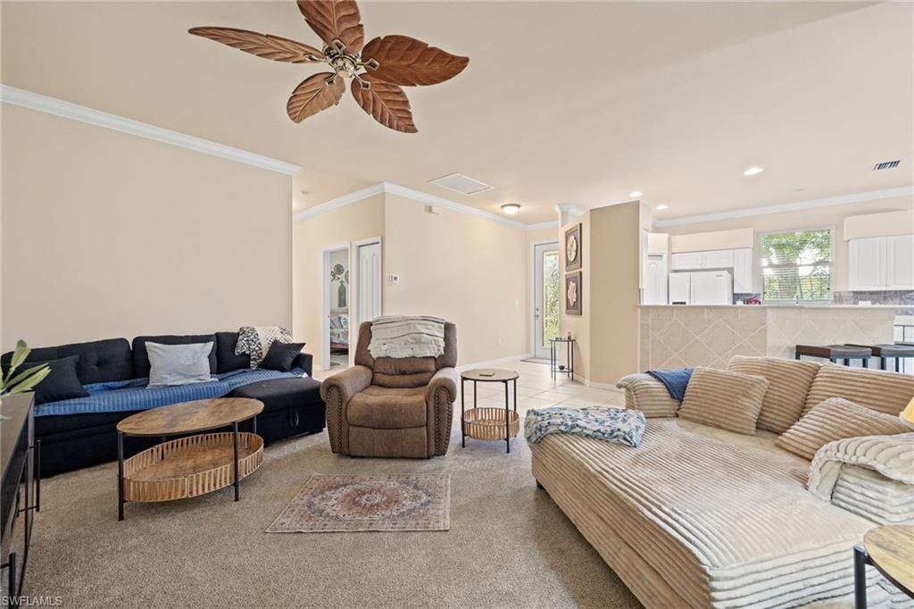 Spacious living area with crown molding, ceiling fan, and carpet flooring
