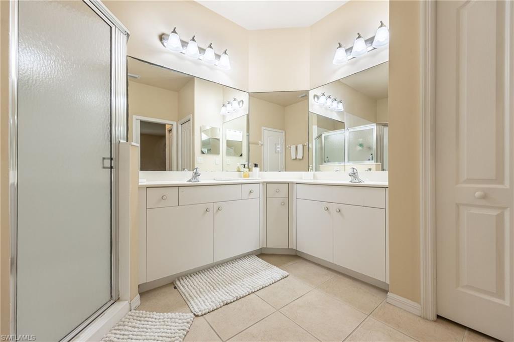 Dual-vanity master bath featuring white cabinetry with ample storage, tile flooring, chrome hardware, and dual illuminated mirrors with sconce lighting