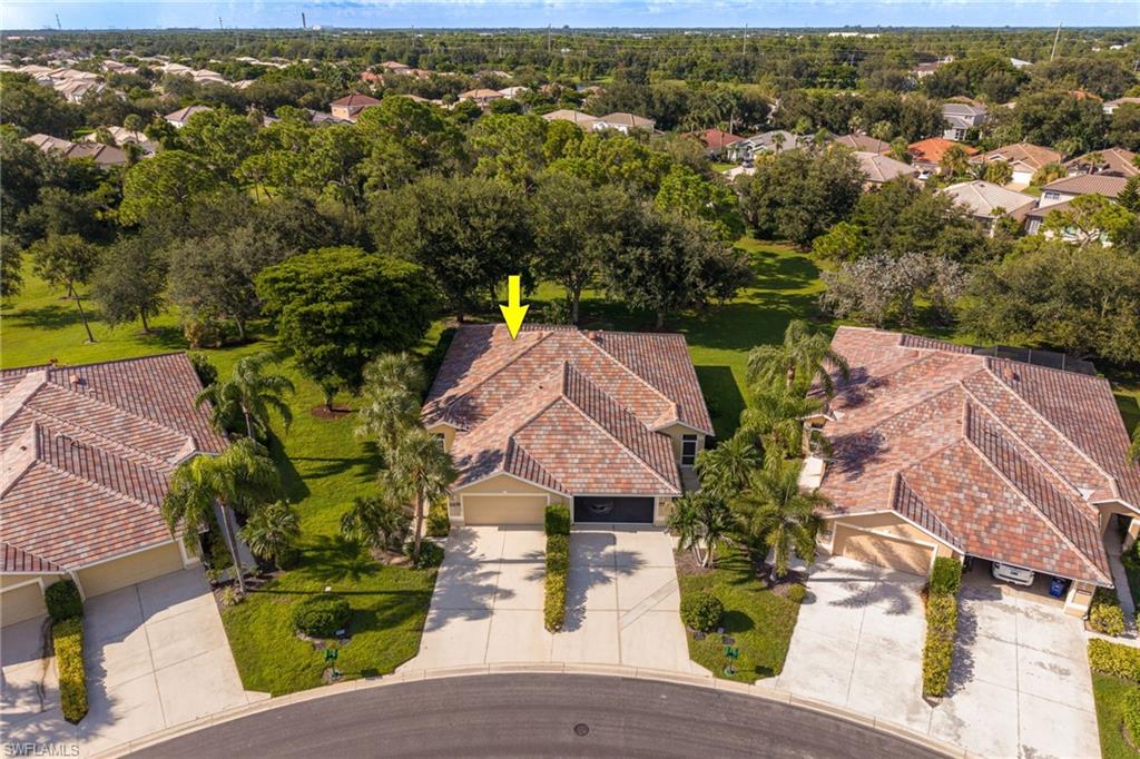 Aerial view showcasing this Mediterranean-style residence featuring a terracotta tile roof, circular driveway with dual entry points, mature landscaping with palm trees and established shade trees, and manicured lawn grounds spanning the expansive property within a tree-lined community setting