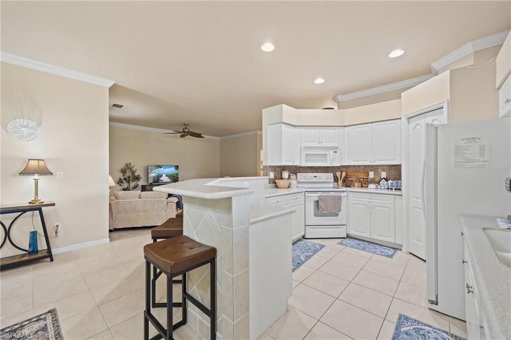 Open kitchen and living area featuring white cabinetry, stainless steel appliances, ceramic tile flooring, and a curved breakfast bar with wood-finish seating