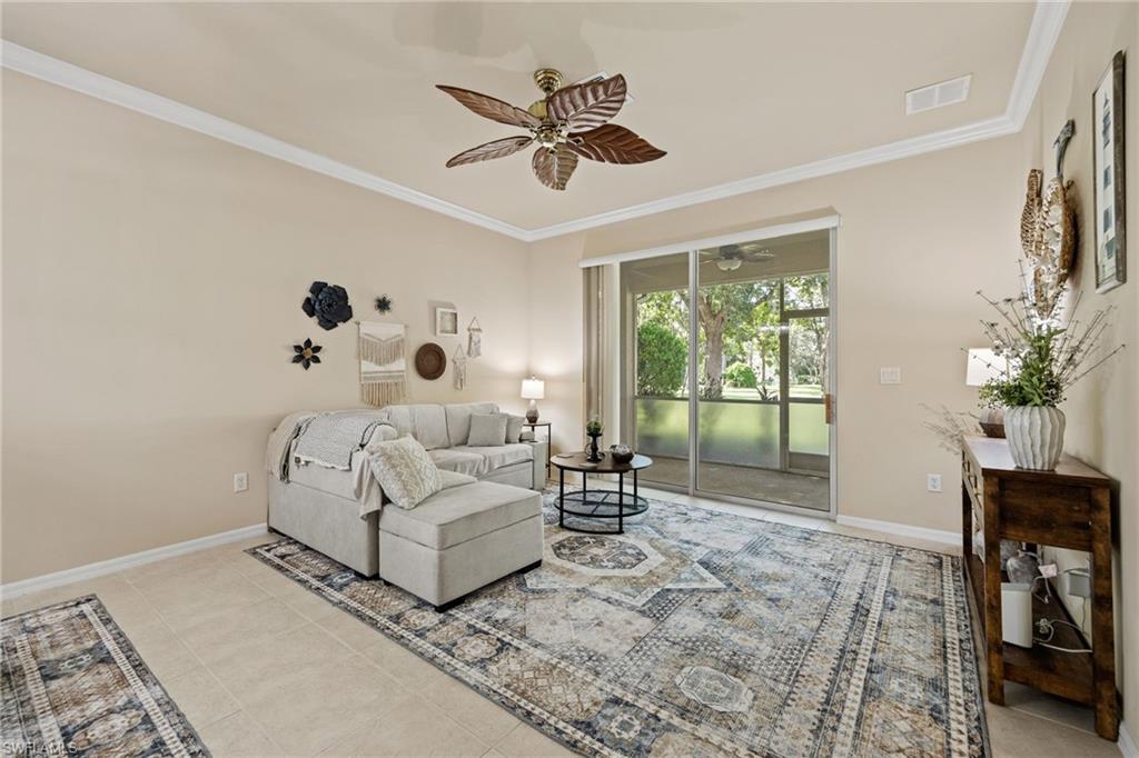 Bright, light-filled room with gleaming tile flooring, coffered ceiling with ceiling fan, and French doors opening to landscaped grounds