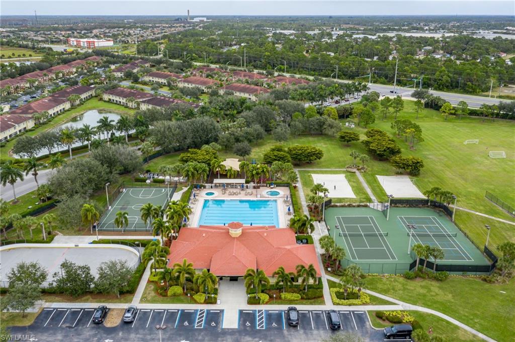 Expansive recreational grounds featuring a resort-style swimming pool with surrounding lounge deck, professional-grade tennis courts, manicured lawn areas, mature landscape plantings including palm trees, and dedicated parking with multiple spaces