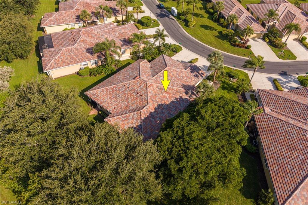 Aerial view showcasing a spacious residential lot with a clay tile roof residence, mature tree landscaping, and manicured grounds surrounded by established neighborhood properties