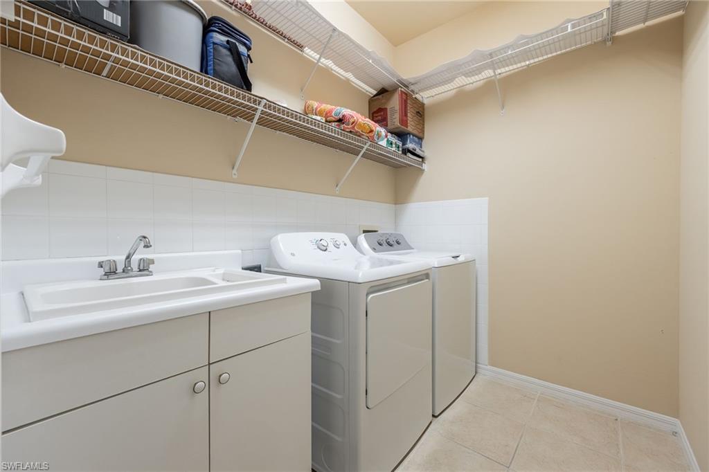 Utility sink with chrome faucet, lower cabinetry, wire shelving, and tiled flooring