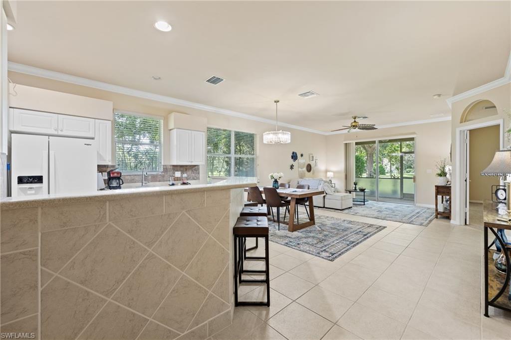 Open-concept kitchen and living area featuring white cabinetry, stainless steel appliances, tile flooring throughout, recessed lighting, and multiple windows providing natural light