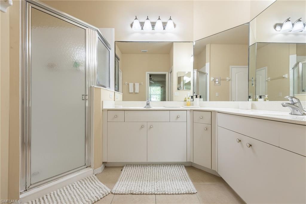 Spa-inspired master bathroom featuring dual vanities with ample storage, large framed mirrors with integrated lighting, tile flooring, and a walk-in shower enclosure with glass doors