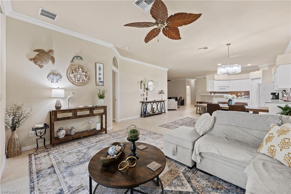 Open-concept living area with light-toned wall finishes, crown molding, a decorative ceiling fan, and recessed lighting
