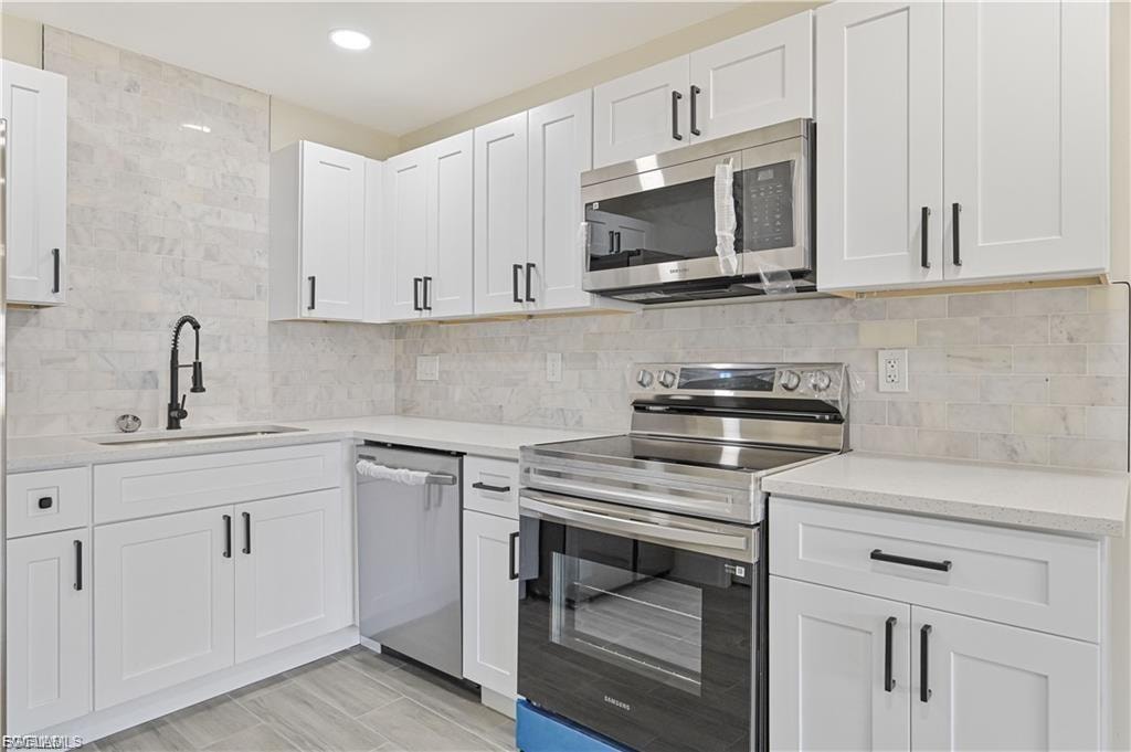 Modern kitchen featuring crisp white cabinetry with black hardware, stainless steel appliances including a gas range and microwave, quartz countertops, subway tile backsplash, a stainless steel sink with matte black faucet, and wood-finish flooring throughout