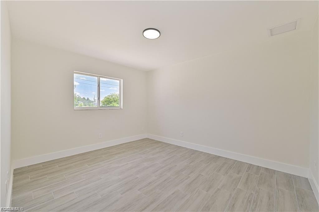 Bright, light-filled bedroom showcasing wood-finish flooring, recessed ceiling lighting, and a dual-window configuration allowing natural illumination