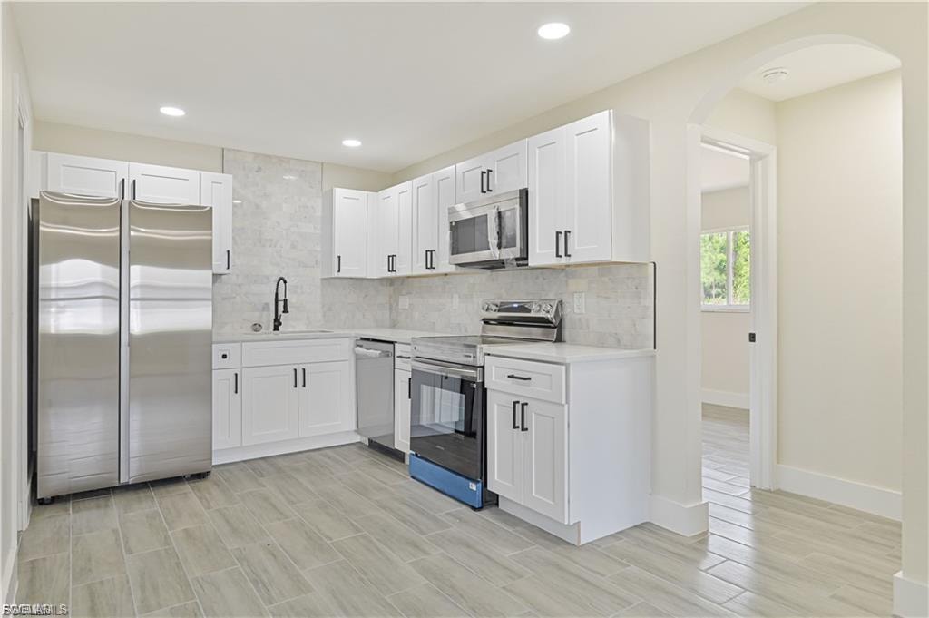 Modern kitchen featuring white cabinetry with hardware accents, stainless steel appliances including a side-by-side refrigerator and gas range, marble subway tile backsplash, wood-finish flooring, and recessed ceiling lighting throughout the space