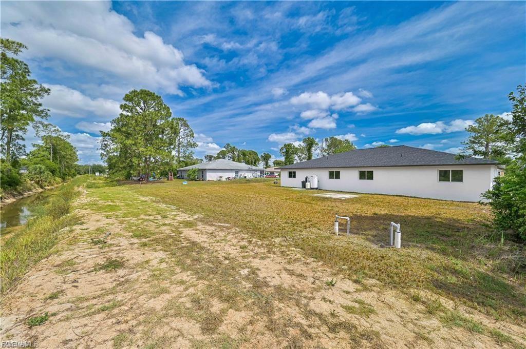 Spacious rural property featuring a modern single-story residence with clean white exterior and dark roof, situated on expansive grounds with mature trees lining the perimeter and open lawn areas ideal for outdoor space or future development