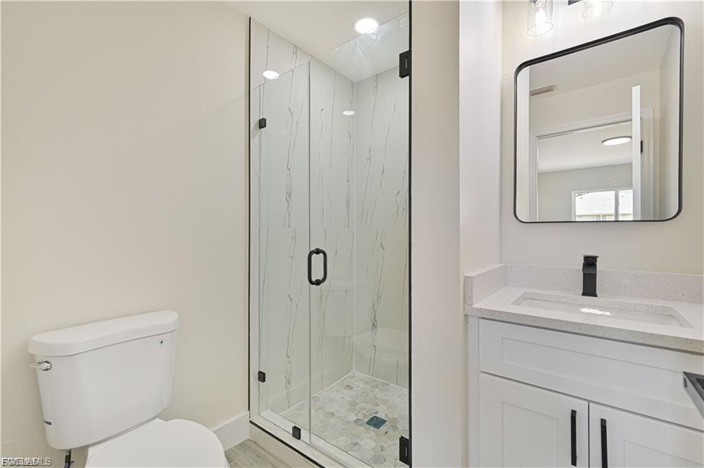 Glass-enclosed shower with tiled walls and floor, single vanity with light-colored countertop, and modern rectangular mirror