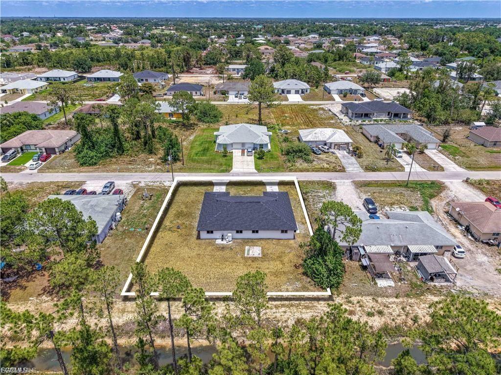 Aerial view showcasing a modern residence with dark solar panel roof array, situated on an expansive cleared lot with mature tree-lined perimeter
