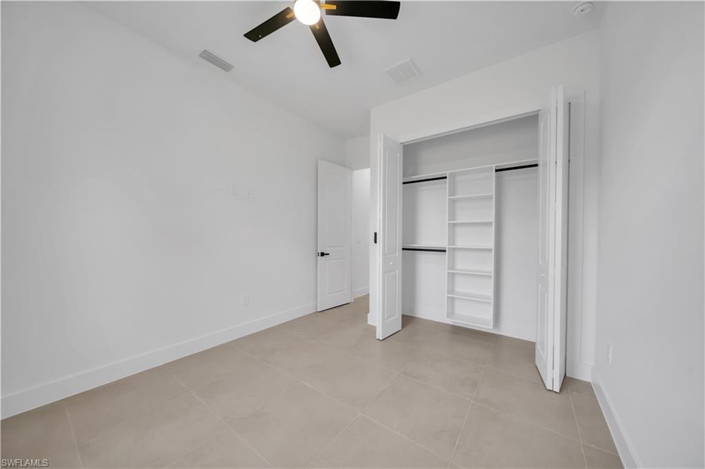 Light-toned tile flooring, ceiling fan with light fixture, bifold closet doors, built-in closet shelving, and a panel door with dark hardware