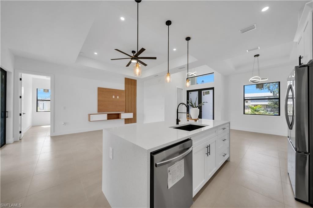 Spacious open-concept living area featuring an expansive kitchen island with a white countertop and dark sink, stainless steel appliances, and a wood-finish wall panel with shelving