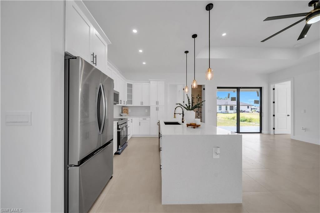 Open-concept kitchen featuring white cabinetry, a large kitchen island with pendant lighting, stainless steel appliances, and light-toned flooring