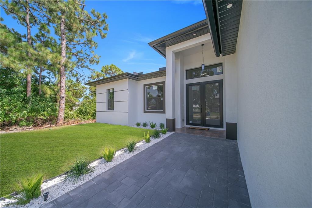 Modern exterior with a stucco finish, dark framed double entry doors, brick paver walkway, and manicured landscaping featuring white stone accents