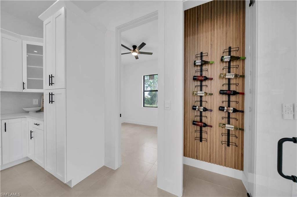 White cabinetry with black hardware, corner countertop, integrated shelving, and a wood-finish accent wall with metal wine racks