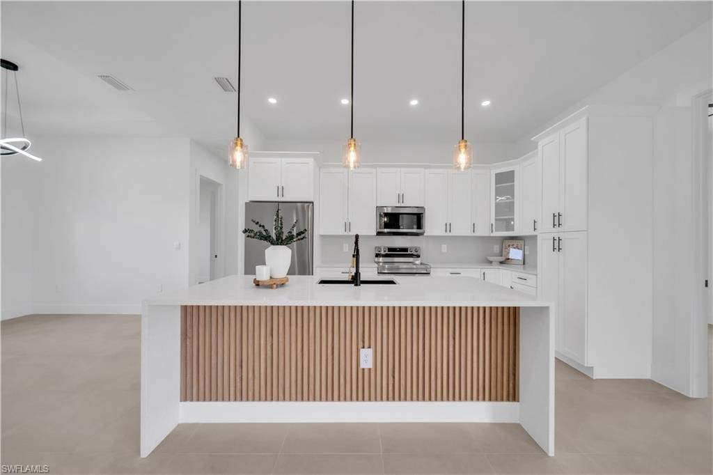 Kitchen featuring white cabinetry, stainless steel appliances, a center island with slat paneling, and pendant lighting