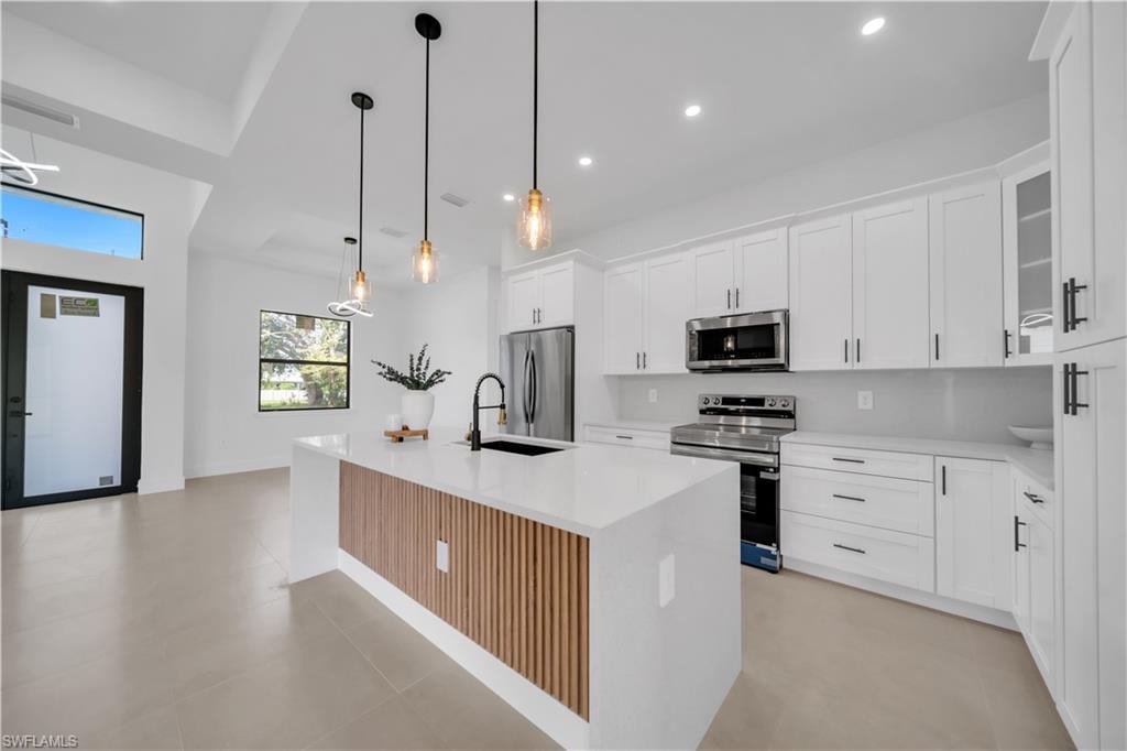 Kitchen featuring an island with wood-slat detail, white cabinetry, stainless steel appliances, and pendant lighting