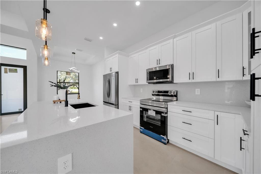 Spacious kitchen featuring white shaker cabinetry, stainless steel appliances, a large island with an undermount sink, pendant lighting, and recessed lighting