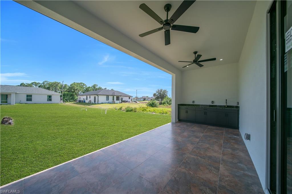 Expansive covered patio with tiled flooring, two ceiling fans, and a built-in cabinetry unit with integrated sink
