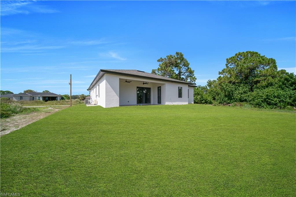 Expansive green lawn bordering a stucco exterior home with a covered patio