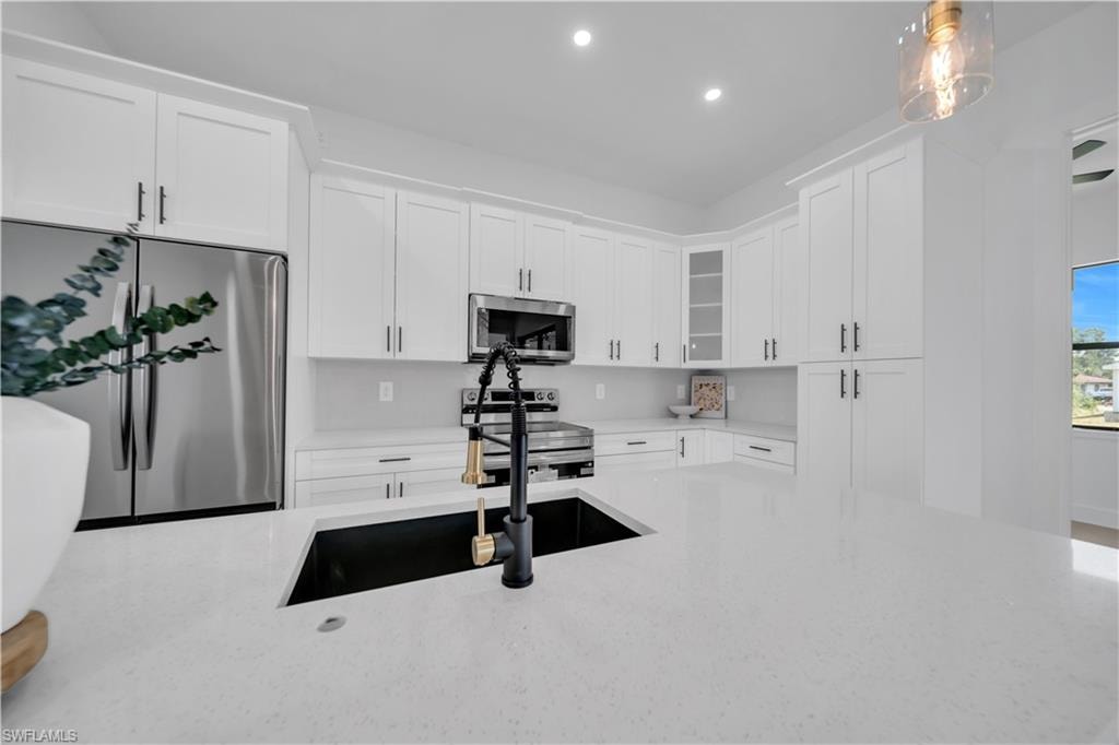 White shaker-style cabinetry, stainless steel appliances, black undermount sink, solid surface countertops, and recessed lighting