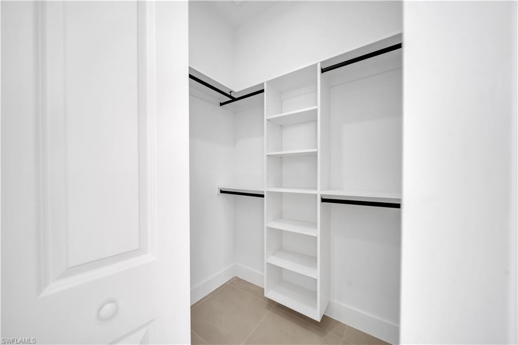 Walk-in closet featuring white built-in shelving, hanging rods, and tile flooring