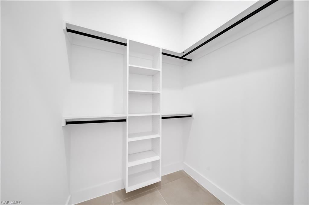 Walk-in closet featuring built-in shelving, multiple hanging rods, and tile flooring