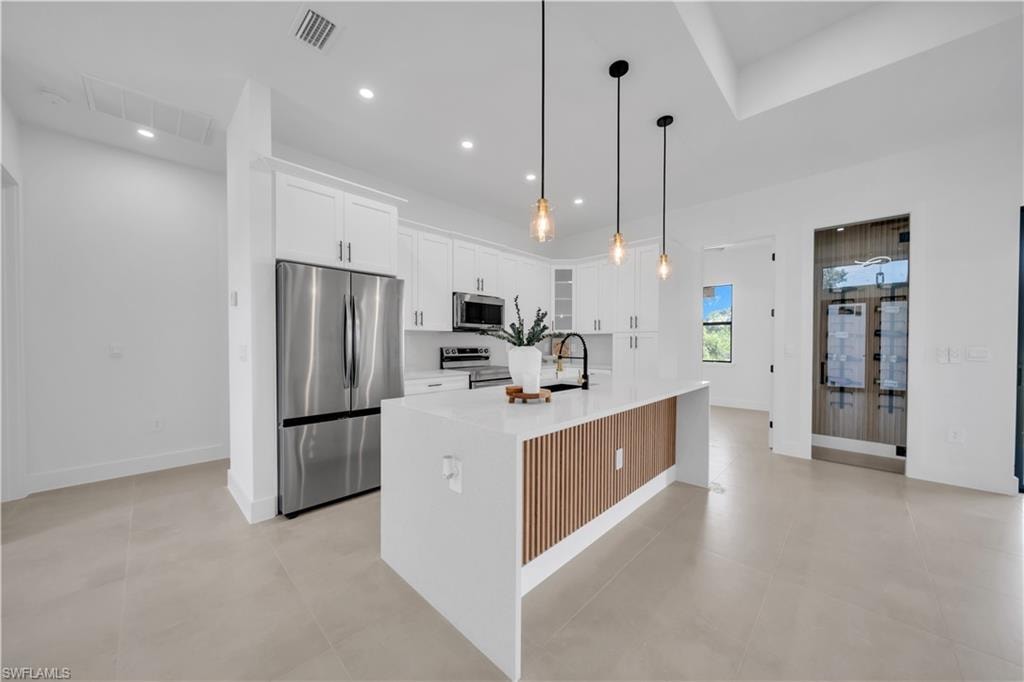 Spacious kitchen featuring white cabinetry, a large center island with wood-finish paneling, stainless steel appliances, and integrated ceiling lighting