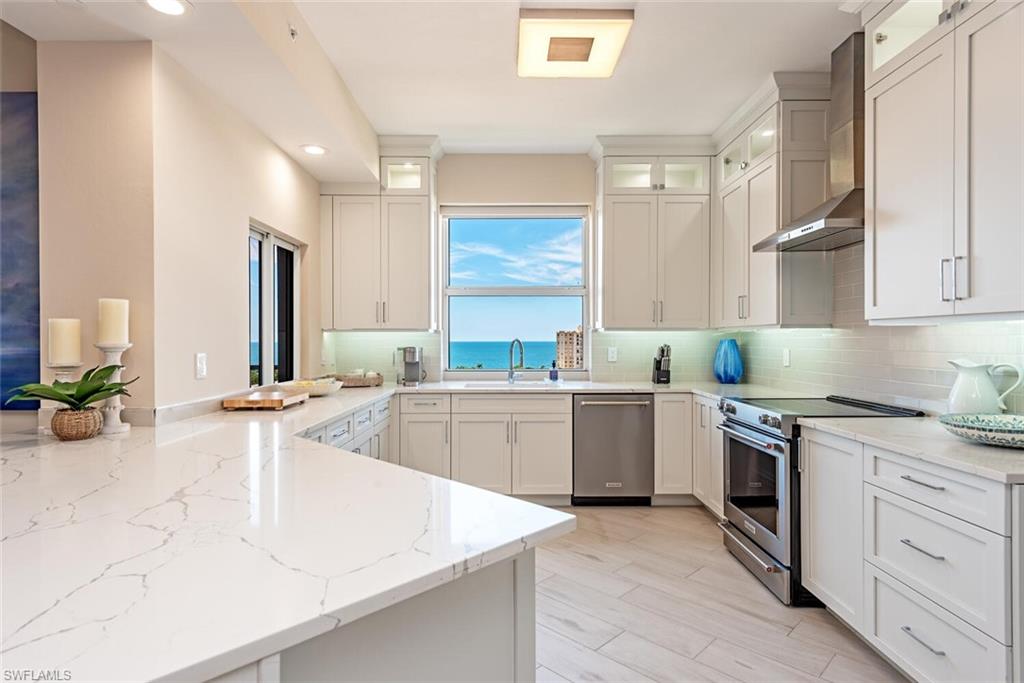 Kitchen featuring appliances with stainless steel finishes, a peninsula, decorative backsplash, light stone countertops, and recessed lighting