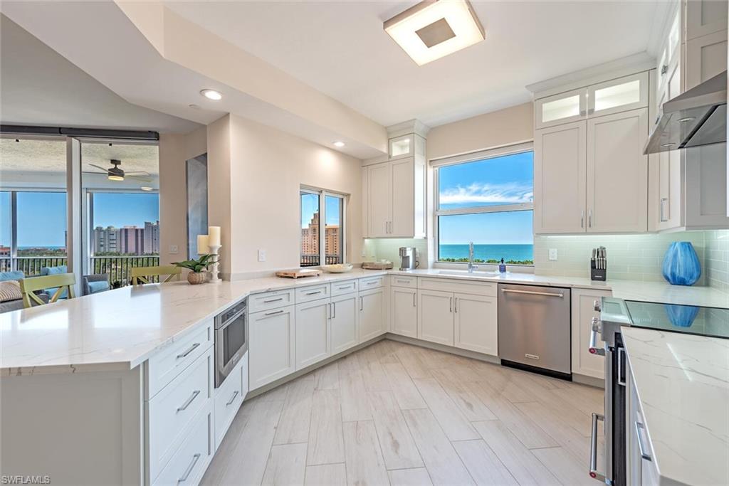 Kitchen with stainless steel appliances, a sink, wall chimney exhaust hood, a peninsula, and white cabinets
