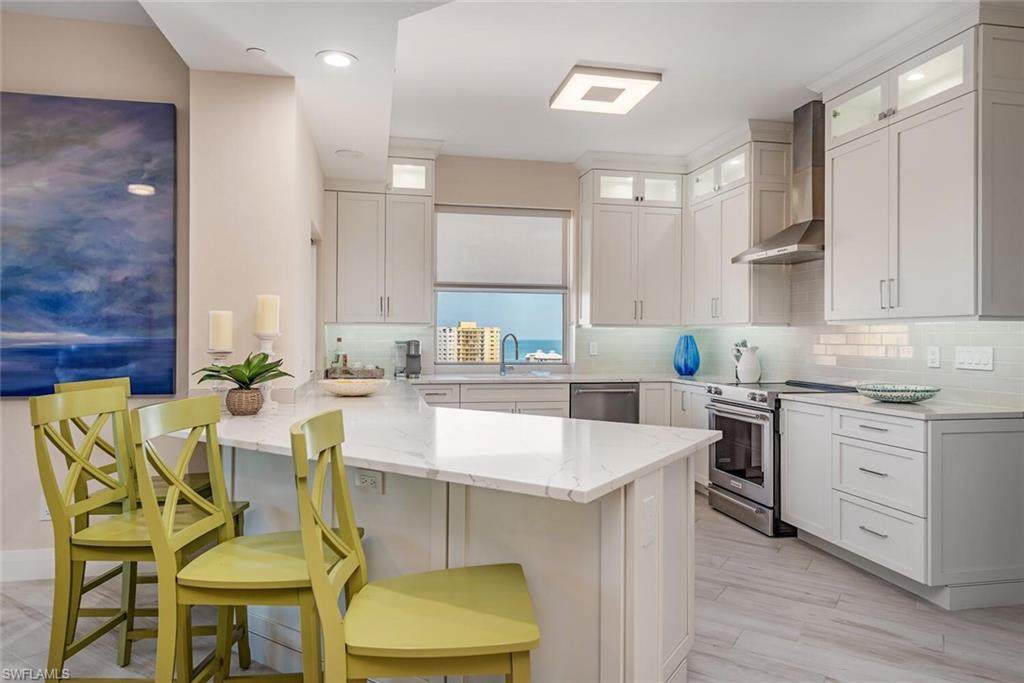 Kitchen featuring stainless steel appliances, wall chimney exhaust hood, a peninsula, light stone countertops, and a breakfast bar