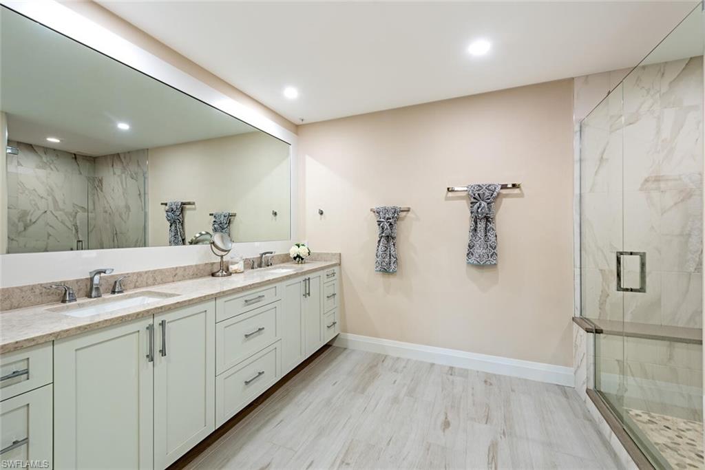 Bathroom with double vanity, a marble finish shower, recessed lighting, baseboards, and wood finished floors