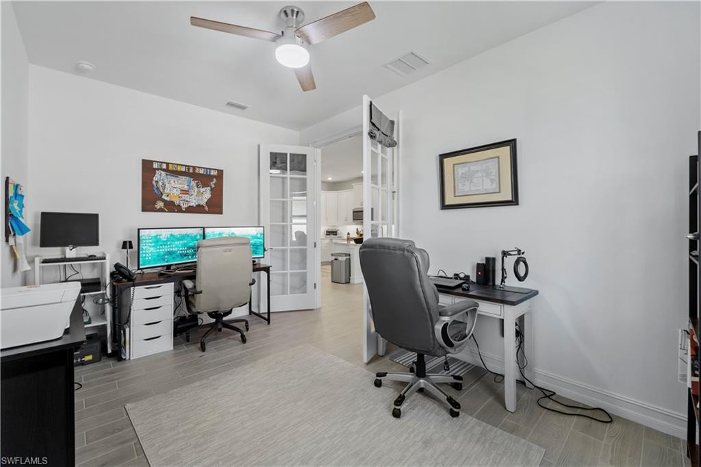 Spacious room featuring wood-finish tile flooring, a ceiling fan with integrated lighting, and French doors