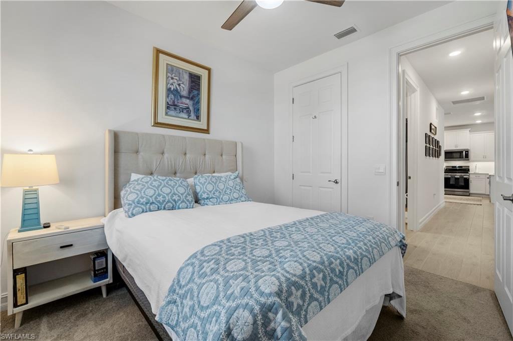 White walls with a ceiling fan, a tufted headboard, and a white nightstand with a drawer